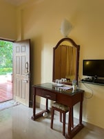 Una habitación con un escritorio de madera, un espejo, un televisor y una puerta que da al exterior.
