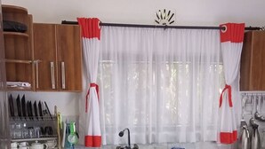 A kitchen with wooden cabinets, a marble countertop, a sink, and a window with white curtains. - Lux Suites Siyoi Gardens Kitale (Kitale)