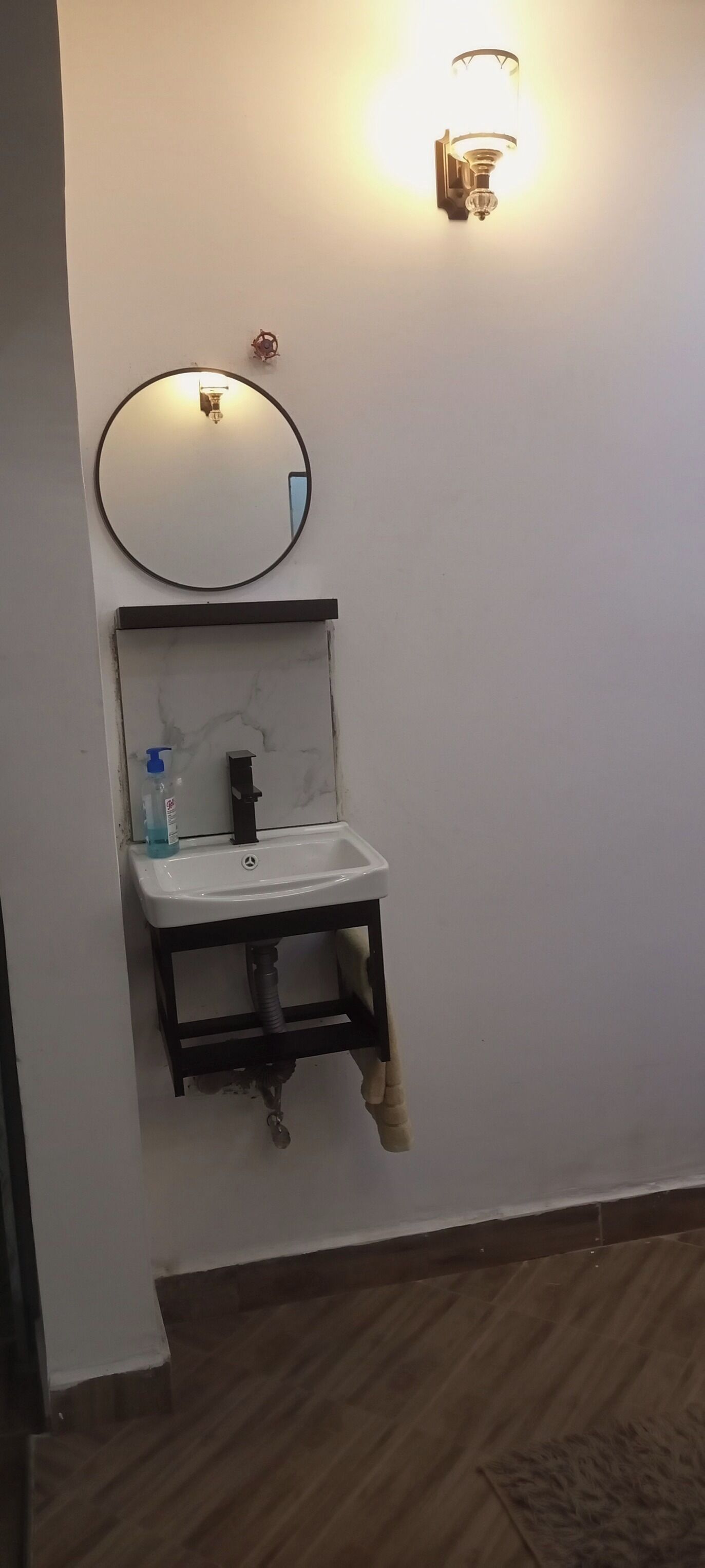 A bathroom with a white sink, a round mirror, and a wall-mounted light fixture.