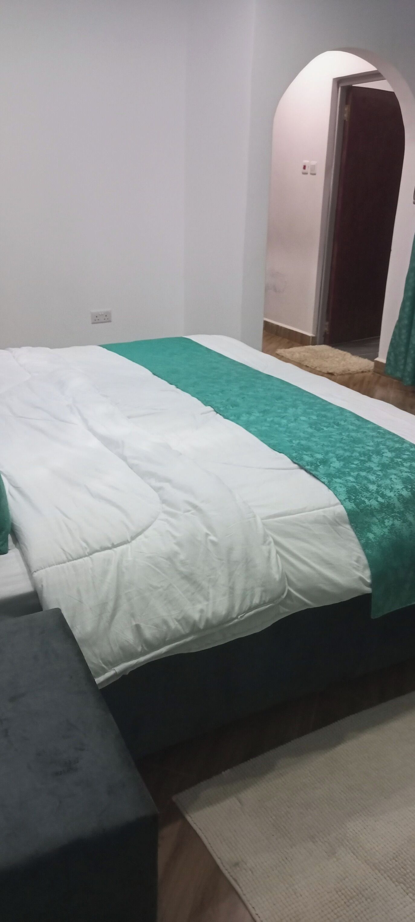 Un lit avec une couvre-lit blanche et verte, une tête de lit sombre et une petite table de chevet.
