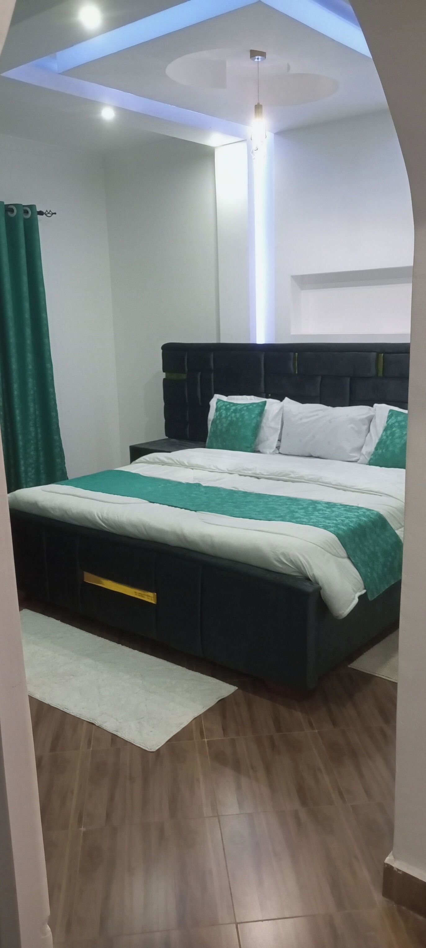 A bedroom with a bed, a nightstand, a green curtain, and a white rug.