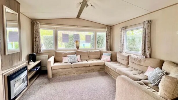 Una habitación acogedora con un amplio sofá seccional beige, una chimenea y ventanas grandes con cortinas.