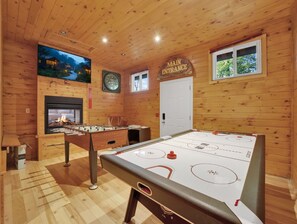 A wooden-floored room with a foosball table, a fireplace, a clock, and a window.