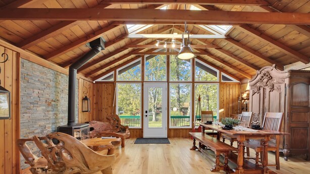 Ein rustikales Holzinterieur mit hohen Decken, einem Kamin, einem Essbereich und großen Fenstern.