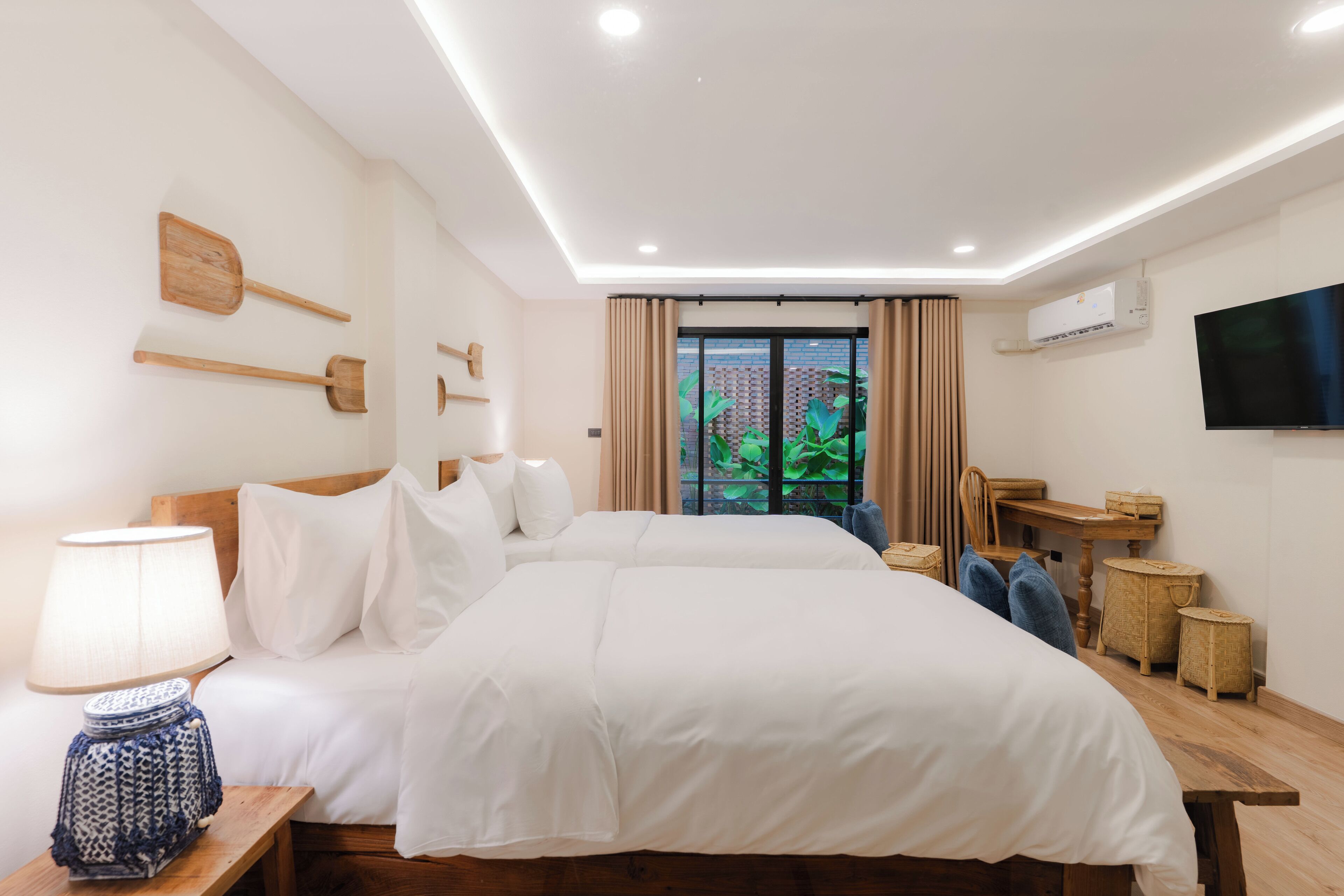 A hotel room with two beds, a desk, a chair, a TV, and a window with curtains.