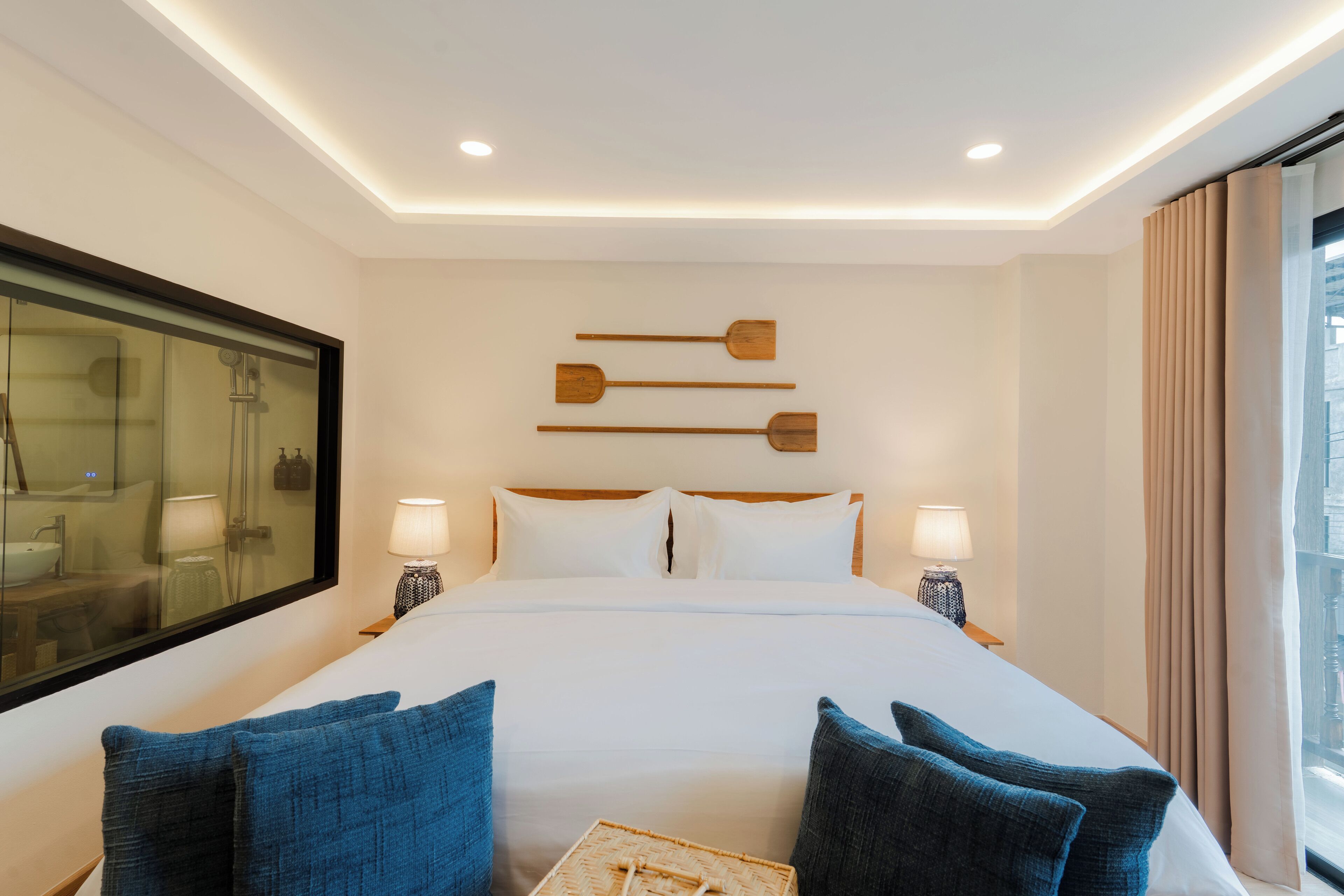 A hotel room with a large bed, two bedside lamps, a headboard with wooden paddles, a large mirror, and a view of the city through the window.