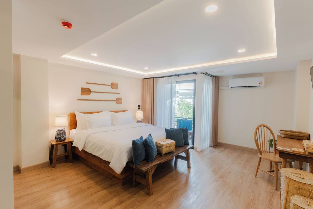 Une chambre moderne avec un grand lit, des tables de chevet, un banc en bois et un bureau avec des chaises.