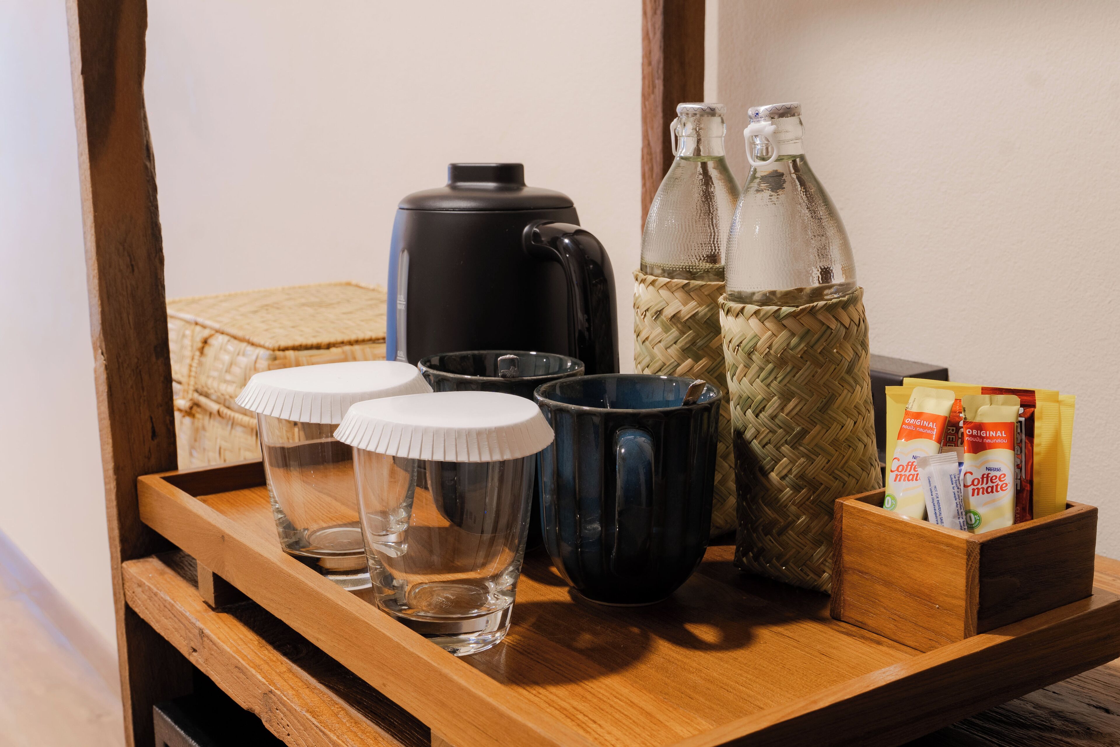 A wooden tray with a coffee maker, two glass mugs, two bottles, and a box of coffee creamer.