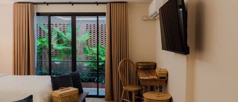 A hotel room with a bed, a wooden table with chairs, a small table with a basket, and a TV mounted on the wall.