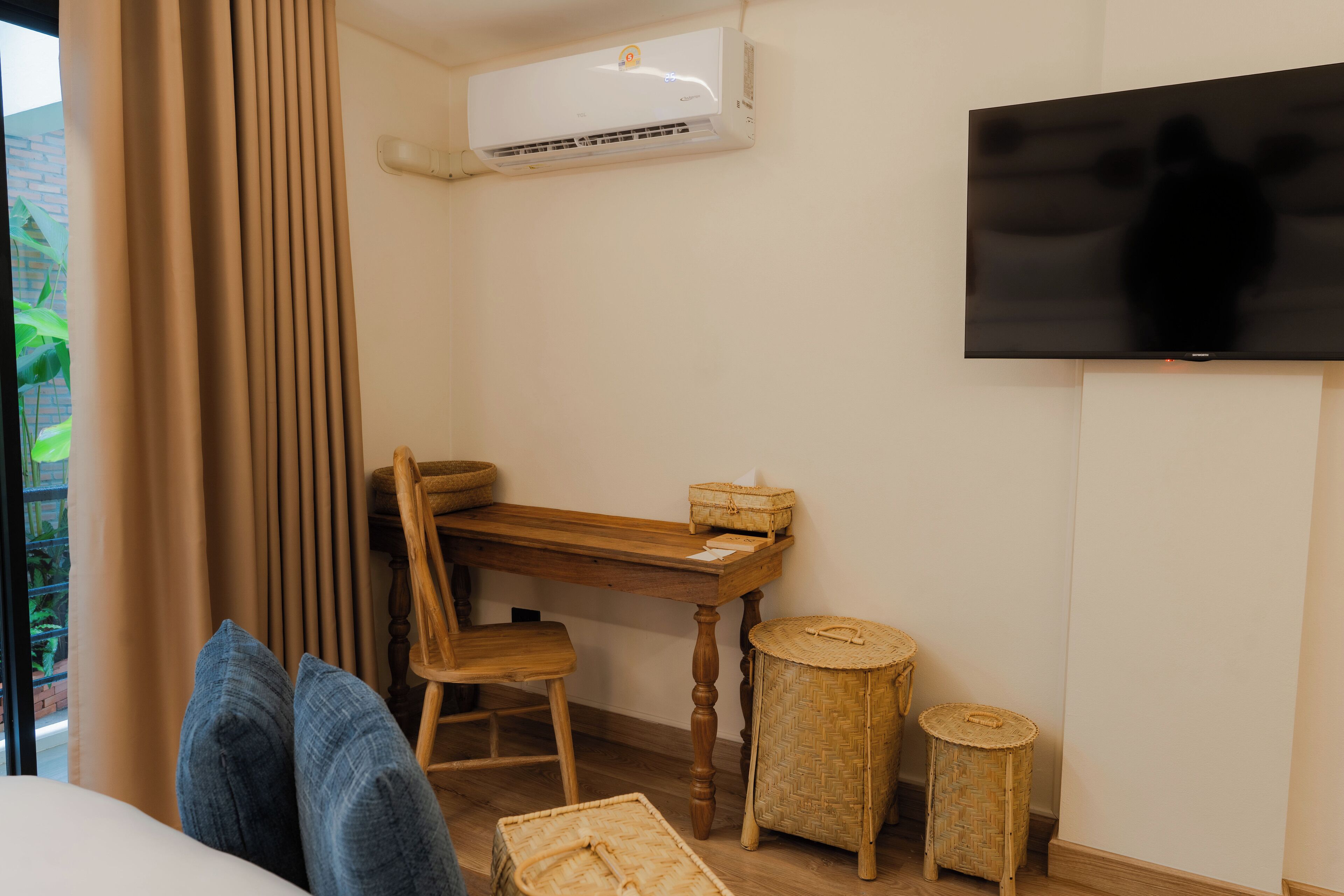 Una habitación con escritorio de madera, una silla, televisor montado en la pared y una ventana con cortinas.