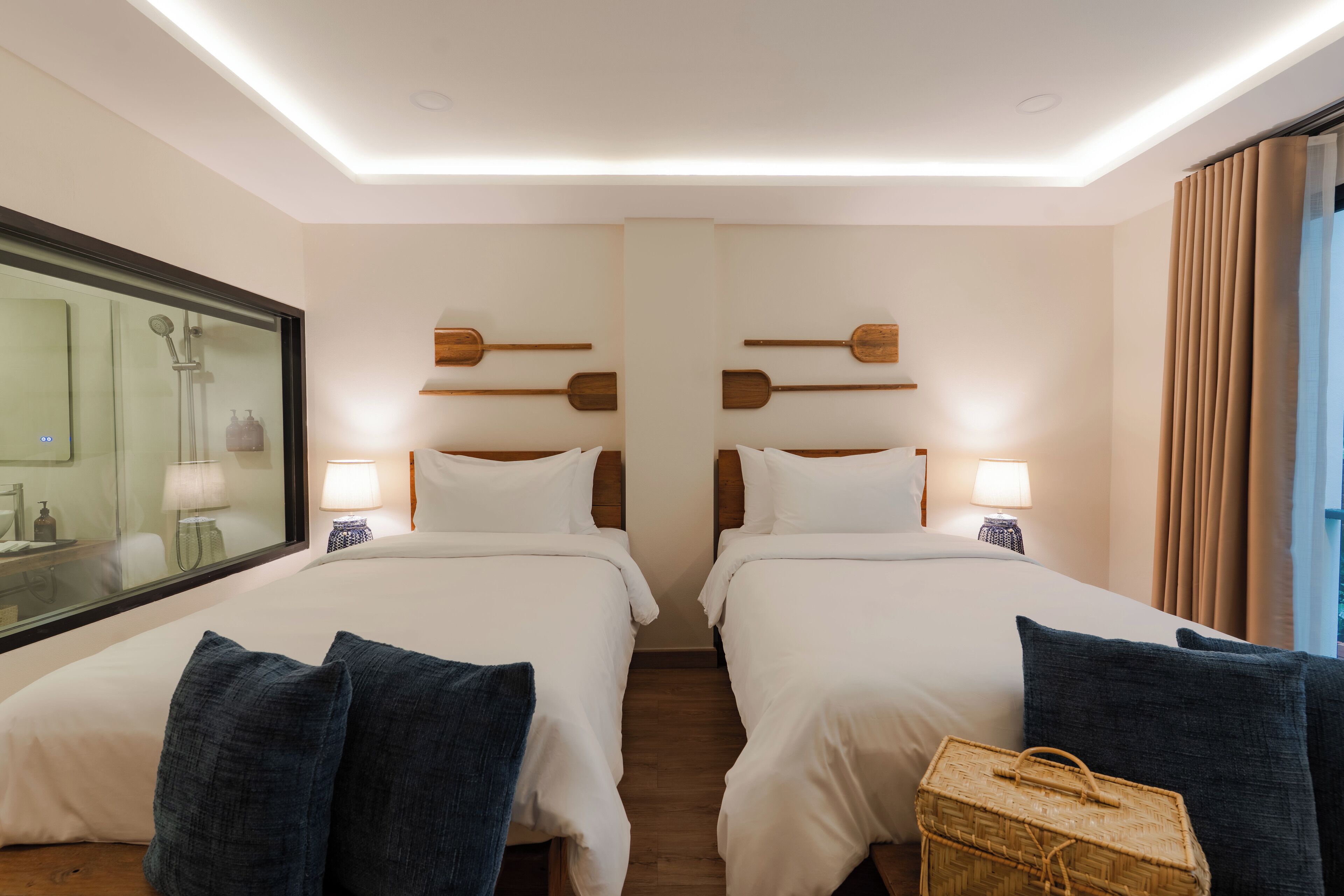Ein Hotelzimmer mit zwei Betten, einem großen Spiegel, Holz-Kopfteilen, Nachttischlampen und einem Korbwäscheschrank.