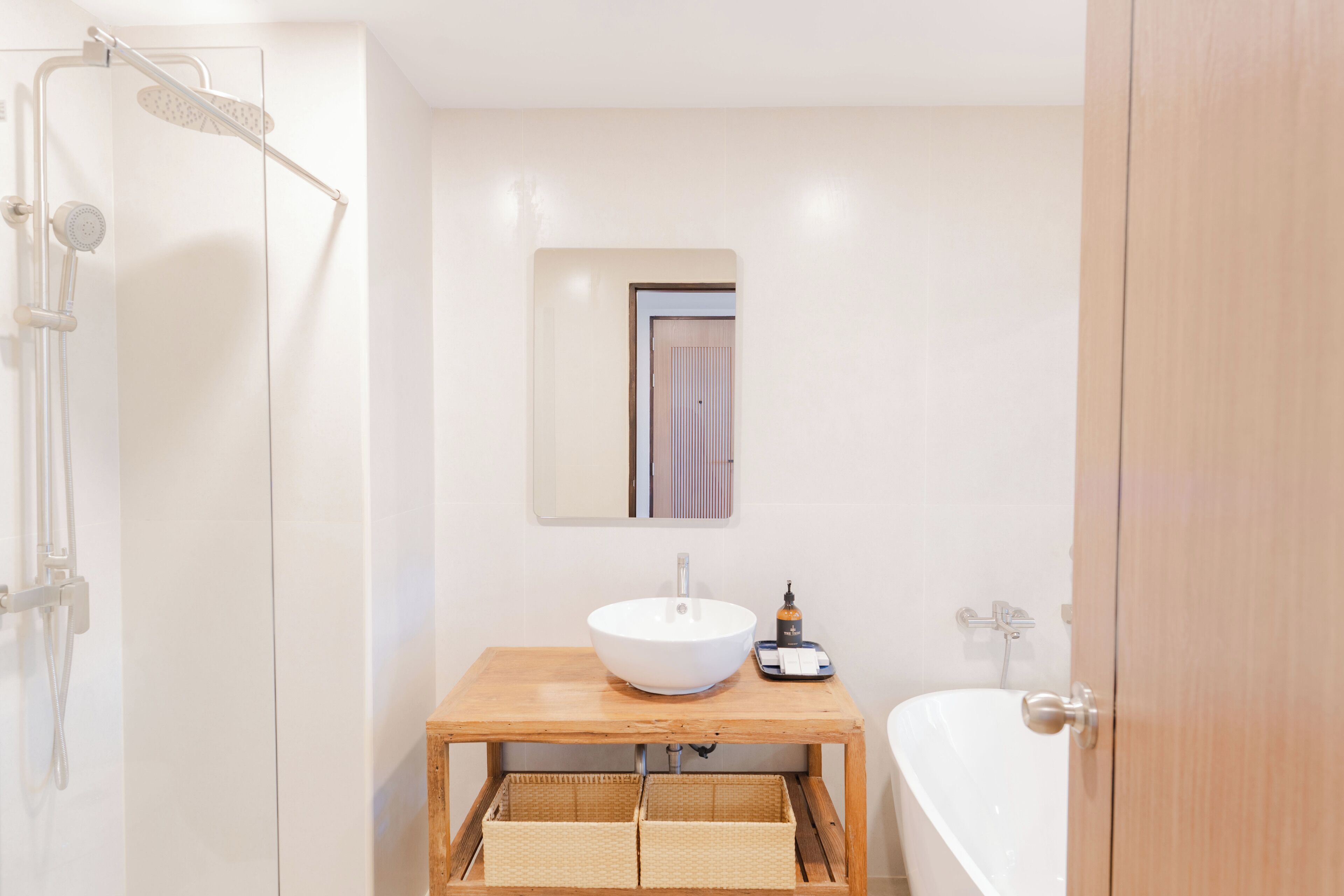 A bathroom with a wooden vanity, a white sink, a mirror, a shower, and a bathtub.