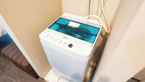 Une machine à laver Haier blanche, dotée d’un réservoir d’eau transparent et reliée à une prise murale par plusieurs câbles.