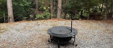 Un espace extérieur circulaire aménagé avec des sièges, comprenant une table et des chaises en métal, entouré d’un chemin de gravier et d’arbres.