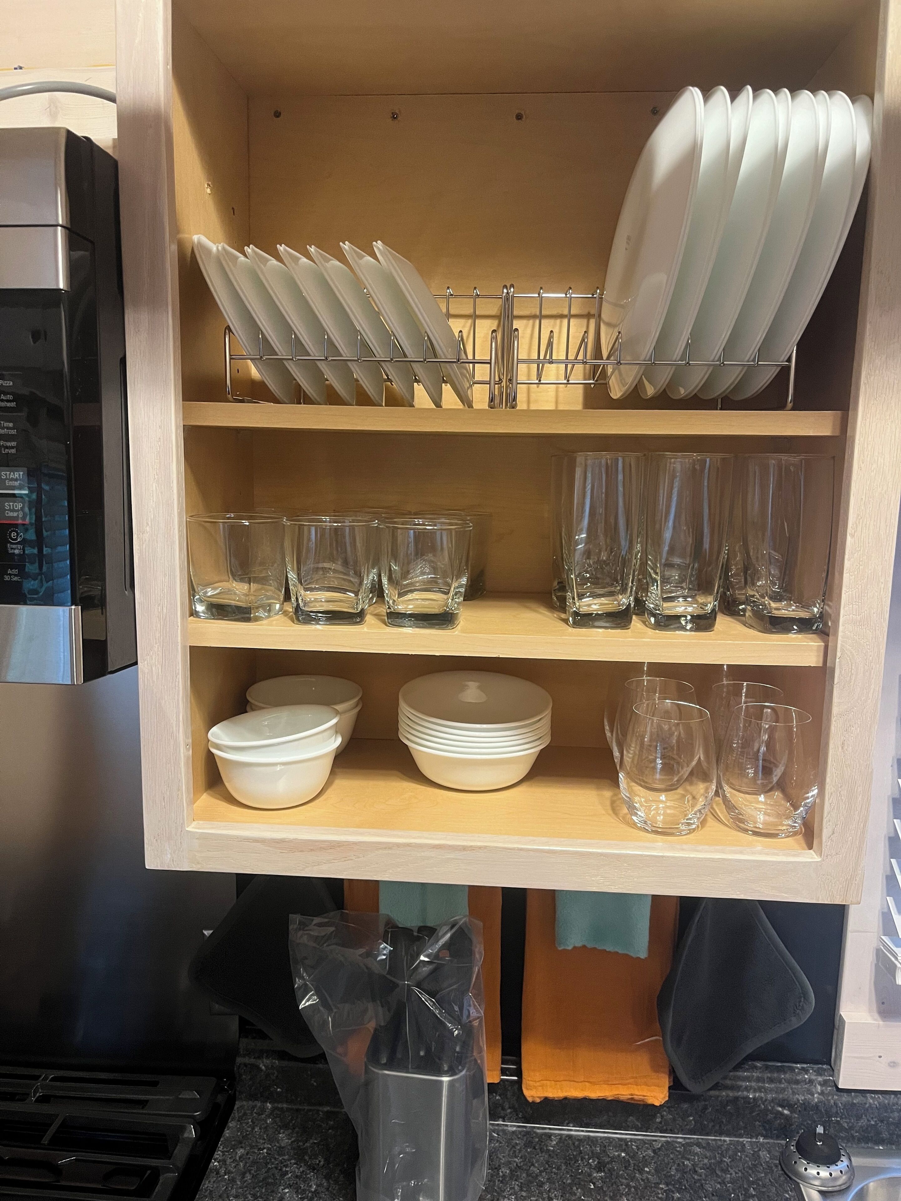 Un pensile della cucina con ripiani che contengono piatti, ciotole e bicchieri.