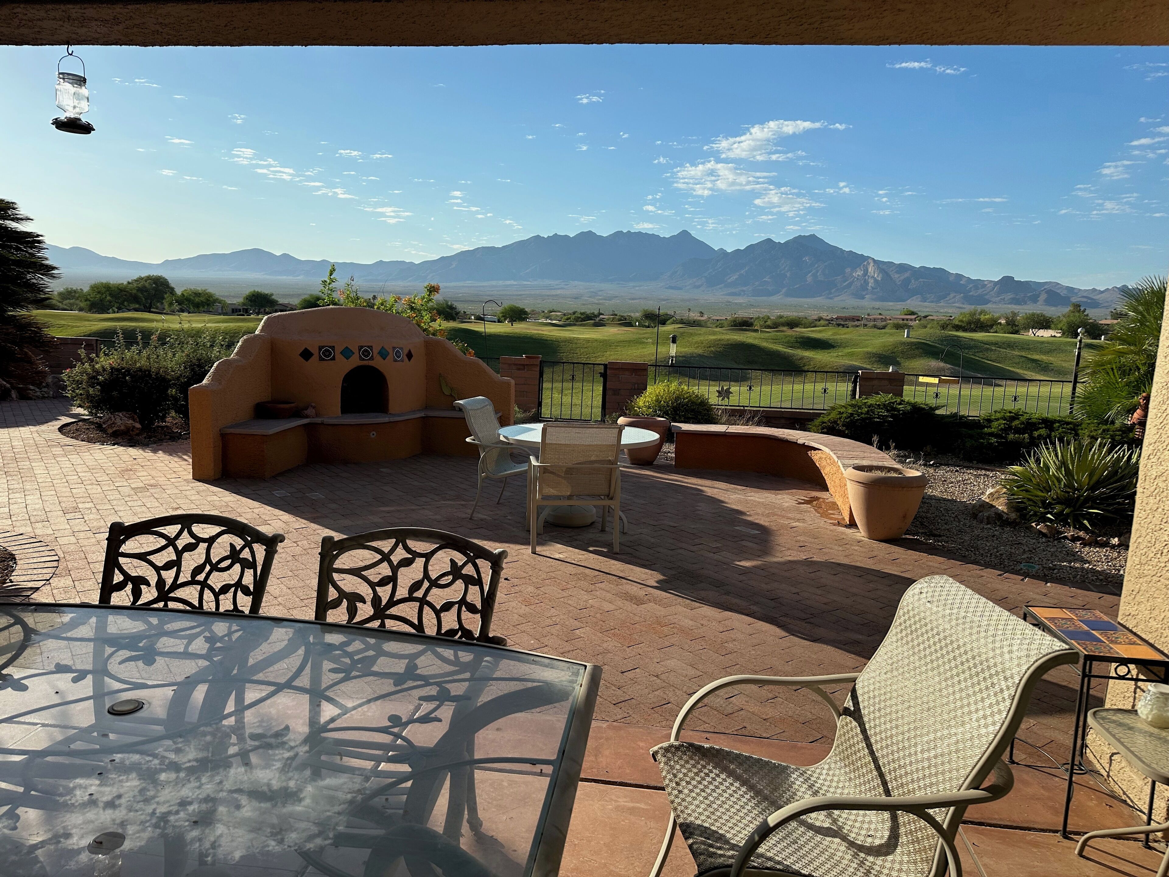 Un patio al aire libre con una mesa de ladrillo, sillas de mimbre, un pequeño horno de ladrillo y vistas a montañas distantes.