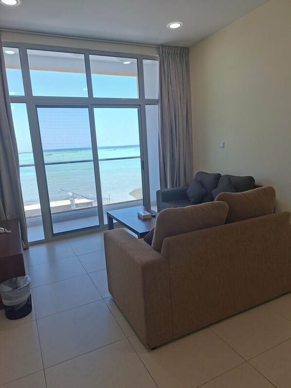 A living room with a sofa, a small table, and a view of the sea through large windows.