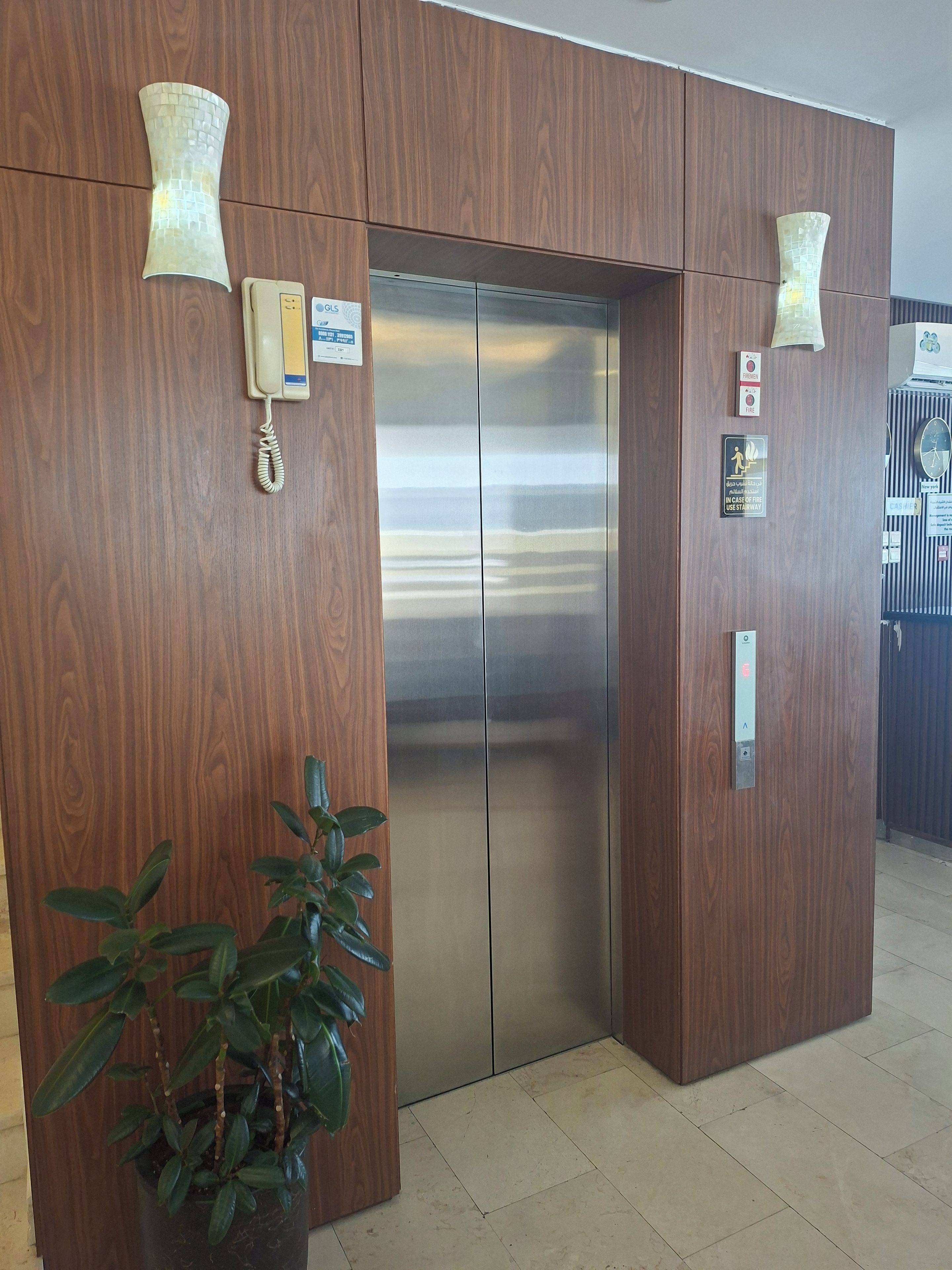 An elevator with a wooden panel design, a wall-mounted phone, and a fire safety sign.