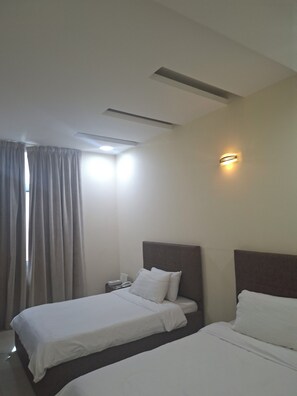 Habitació d'hotel amb dos llits, una tauleta de nit, una làmpada i una finestra amb cortines.