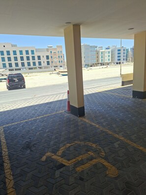 Zona aparcament amb el símbol d'accessibilitat per a persones amb mobilitat reduïda, un piló de formigó i un edifici al fons.