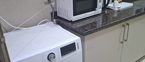 A compact kitchen with a washing machine, microwave, and a countertop with a kettle and utensils.