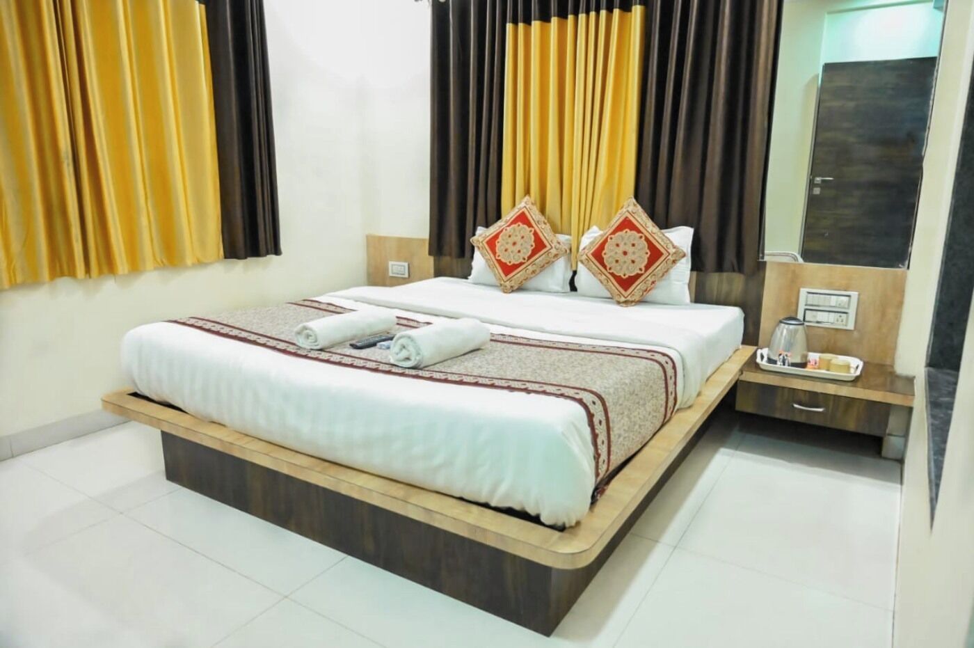 A hotel room with a large bed, a bedside table with a tray, and a mirror.