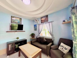 A living room with a sofa, a TV, a table, and a window with curtains.
