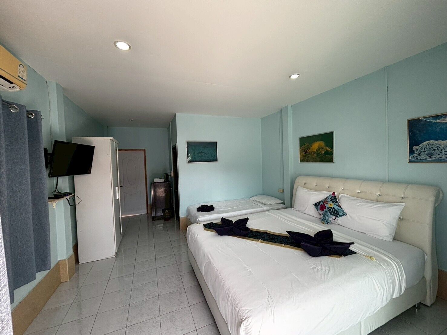 Quarto de hotel com duas camas, televisão, escrivaninha e porta para um corredor.