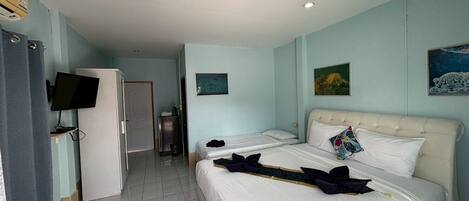Habitación de hotel con dos camas, televisión, escritorio y puerta que da a un pasillo.