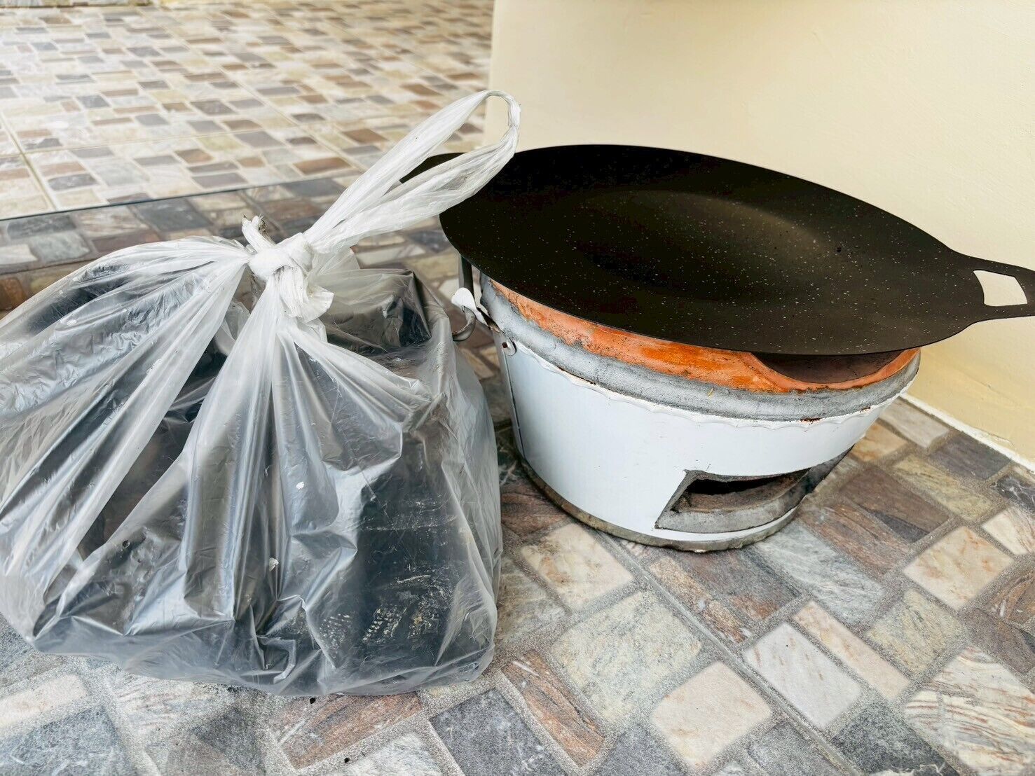 A plastic bag on a tiled floor next to a white pot with a black lid.