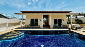 A poolside building with a tiled pool, a covered patio, and a clear blue sky.