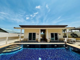 A poolside building with a tiled pool, a covered patio, and a clear blue sky.