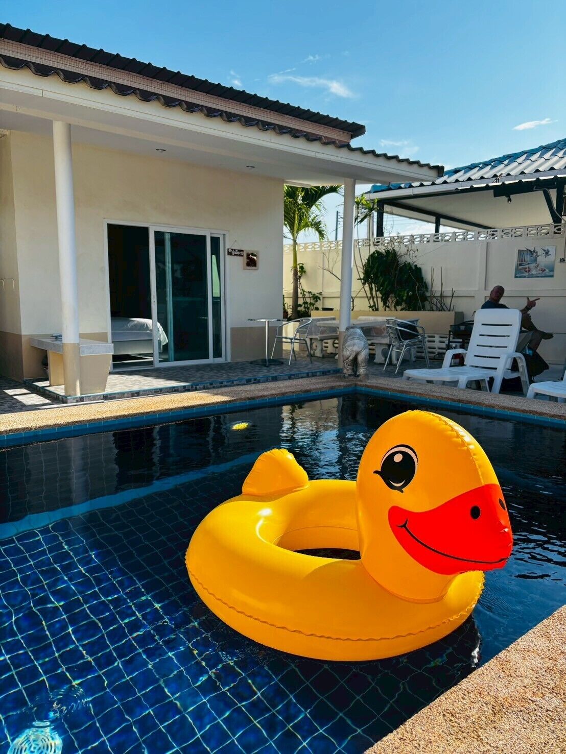 A swimming pool with a yellow inflatable duck float. There is a covered patio area with lounge chairs and a table.