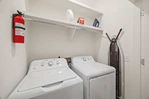 A laundry area with two white washing machines, a fire extinguisher, and a shelf with a kettle and a box.