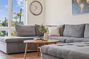 A modern living room with a grey sectional sofa, a round wooden coffee table, and a wall clock.