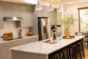 A modern kitchen with grey cabinets, a marble island, pendant lights, and a Christmas tree decoration.