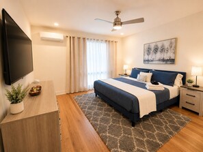 A hotel room with a bed, bedside tables, a TV, a ceiling fan, and a painting on the wall.