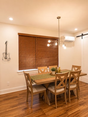 A dining area with a wooden table, chairs, a hanging light fixture, and a guitar on the wall.