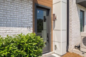 A modern building with a white brick facade, a glass door entrance, and a small green bush in front.