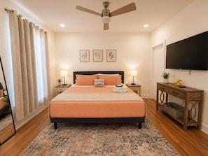 A bedroom with a bed, bedside tables, a ceiling fan, a TV, and a window with curtains.