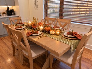 A dining table set for six with wooden chairs, a woven placemat, and autumn-themed decorations.