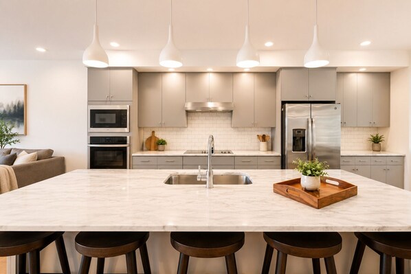 Una cocina moderna con una isla central, electrodomésticos de acero inoxidable, iluminación colgante y un diseño minimalista.
