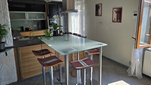 A modern kitchen with a glass dining table, bar stools, and a built-in oven. - Beautiful Alsatian house on the wine route, at the foot of Haut-Koenigsbourg (Rorschwihr)