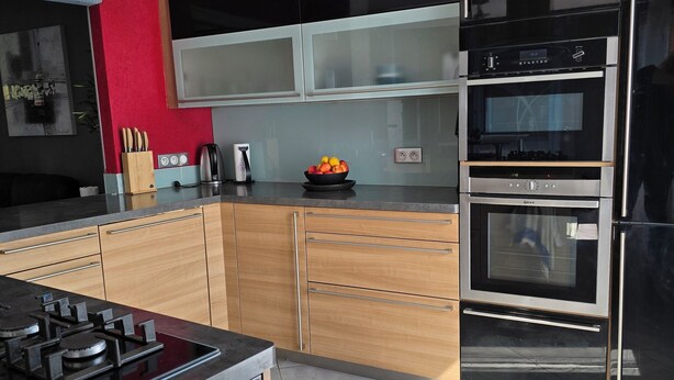 A modern kitchen with a gas stove, stainless steel appliances, wooden cabinets, and a red accent wall. - Beautiful Alsatian house on the wine route, at the foot of Haut-Koenigsbourg (Rorschwihr)