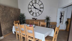 A dining area with a large wall clock, wooden chairs, a table with a white tablecloth, and potted plants. - Beautiful Alsatian house on the wine route, at the foot of Haut-Koenigsbourg (Rorschwihr)