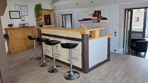 A kitchen with a central island, wooden bar stools, and a stone wall. - Beautiful Alsatian house on the wine route, at the foot of Haut-Koenigsbourg (Rorschwihr)