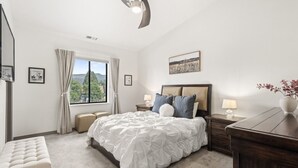 A bedroom with a large bed, a nightstand, a dresser, a window with curtains, and a ceiling fan. - Modern Condo with Sopris Views in Downtown Carbondale (Carbondale)