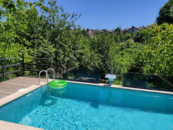 Una piscina con bordo in legno, ringhiere in metallo e un galleggiante gonfiabile verde.