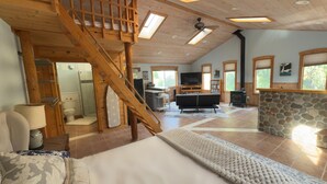 Un vaste espace de vie comprenant un escalier en bois, une cheminée en pierre, une cuisine et une salle de bain.