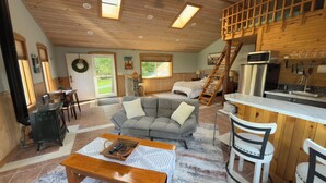 Un intérieur de chalet chaleureux comprenant un salon, une cuisine et une chambre à coucher située en mezzanine.